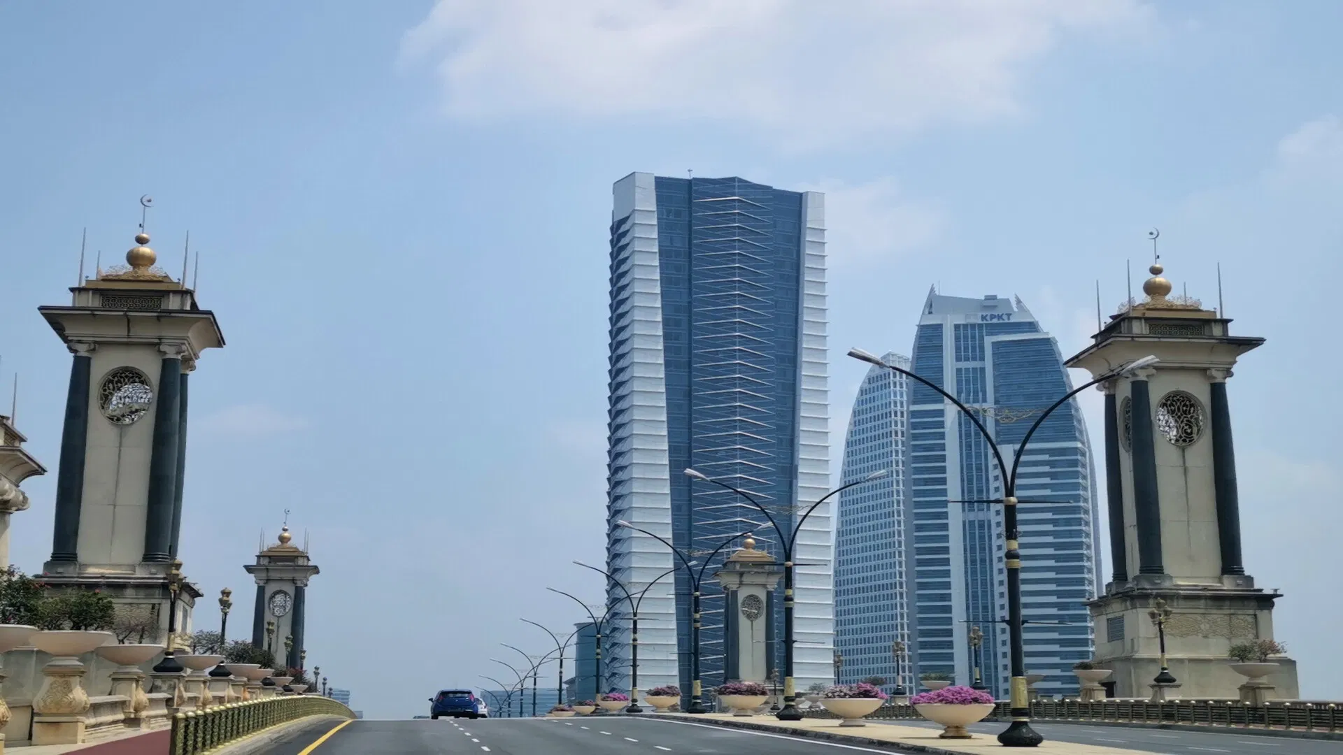 A car on a wide Putrajaya boulevard, between the ornamental towers of the Putra Bridge